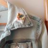broche mots fleuris enveloppe blanche remplie de fleurs colorées en argile polymère présentée sur une veste en jean